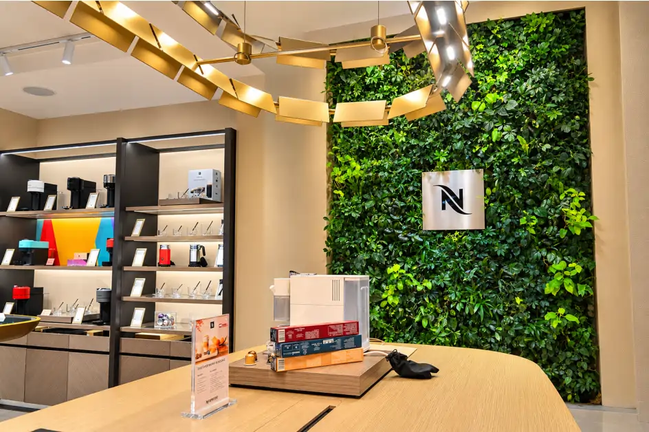 Indoor greenwall tinggi di ruang pamer mesin kopi dengan rak display dan lampu gantung emas