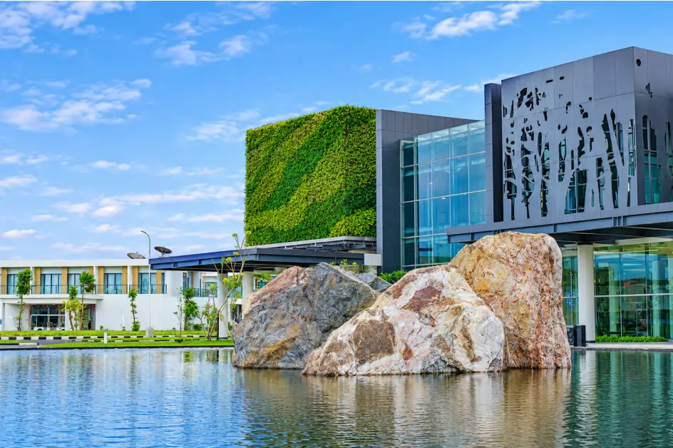 Vertical garden pada fasad gedung modern dengan kolam reflektif dan batu besar di bagian depan